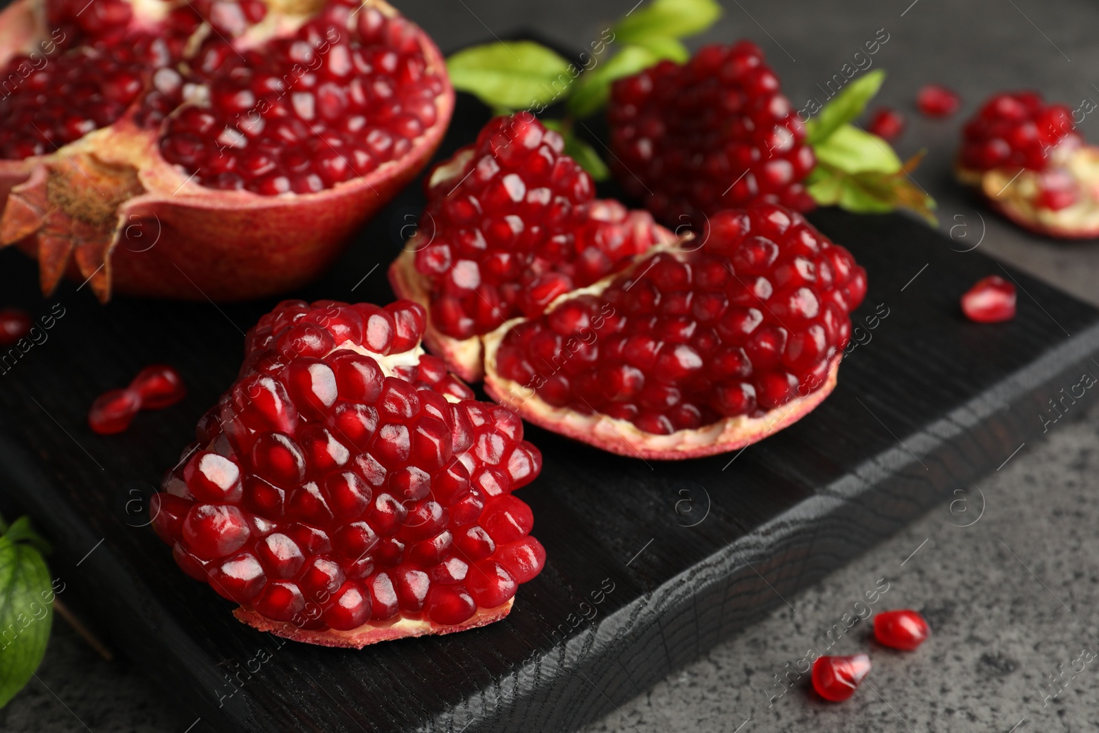 Photo of Cut fresh pomegranate and green leaves on grey table, closeup