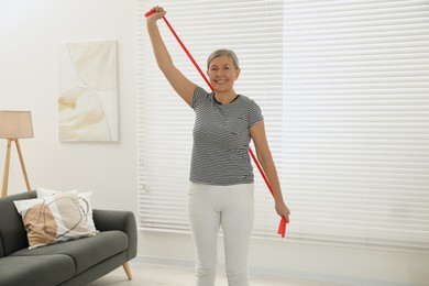 Photo of Senior woman doing exercise with fitness elastic band at home