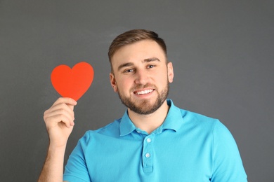 Young man with paper heart on grey background