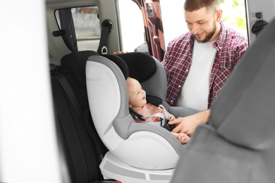 Father fastening baby to child safety seat inside of car