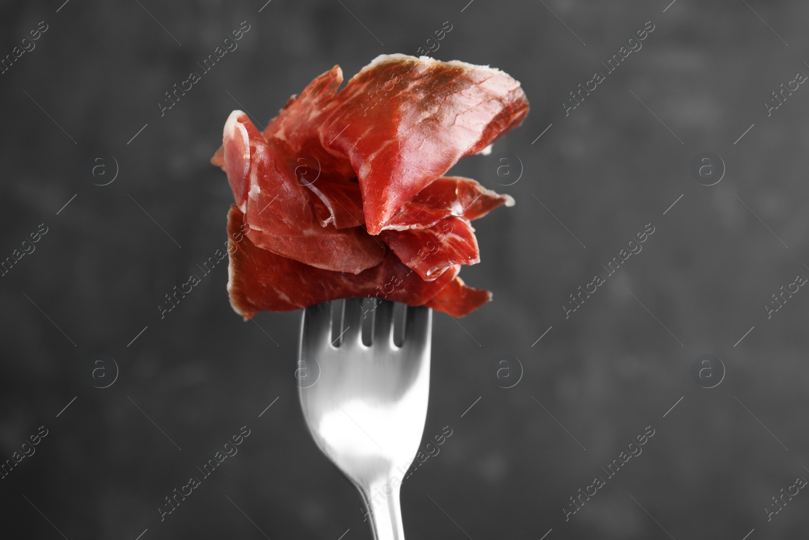 Photo of Tasty prosciutto on fork against grey background, closeup