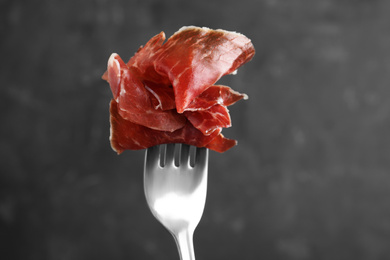 Photo of Tasty prosciutto on fork against grey background, closeup