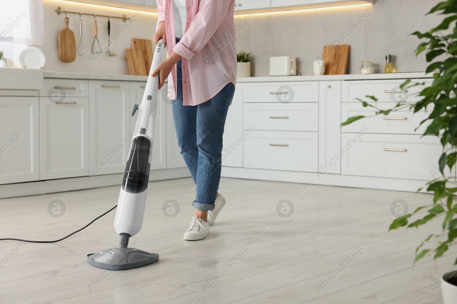 Photo of Woman cleaning floor with steam mop in kitchen at home, closeup. Space for text