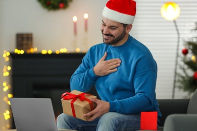 Photo of Celebrating Christmas online with exchanged by mail presents. Man thanking for gift during video call on laptop at home