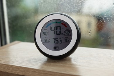 Digital hygrometer with thermometer near window on rainy day, closeup