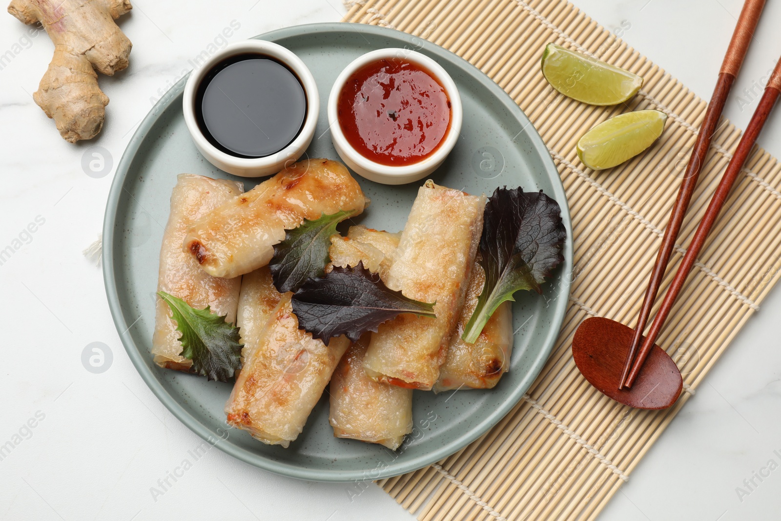 Photo of Tasty fried spring rolls, lettuce, sauces and other products on white marble table, flat lay