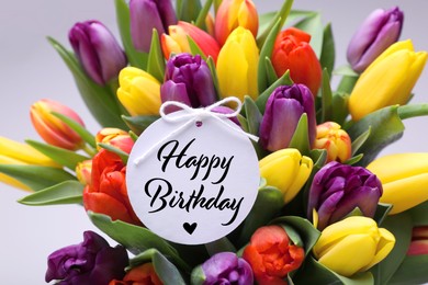 Image of Beautiful bouquet of tulip flowers with Happy Birthday card on light background, closeup