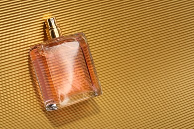 Luxury women's perfume. Sunlit glass bottle on golden surface, top view. Space for text