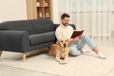 Man reading book on floor near his cute Labrador Retriever at home