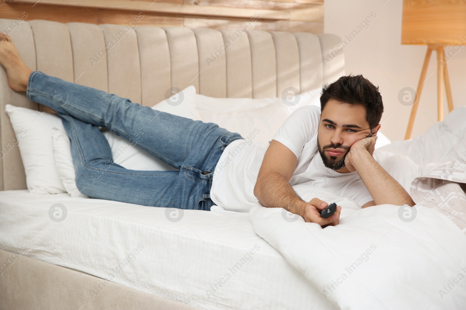 Photo of Lazy young man watching TV on bed at home