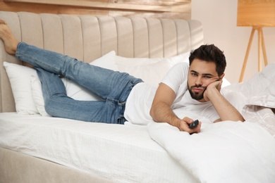 Lazy young man watching TV on bed at home