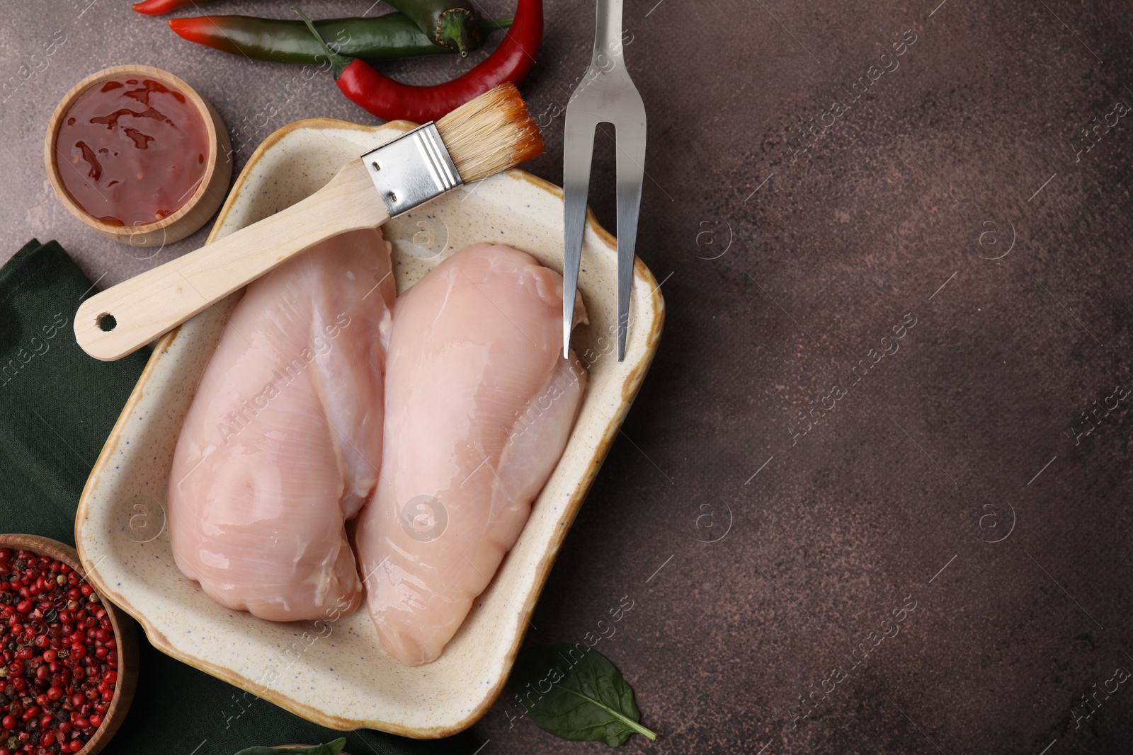 Photo of Marinade, basting brush, raw chicken fillets and spices on brown table, flat lay. Space for text