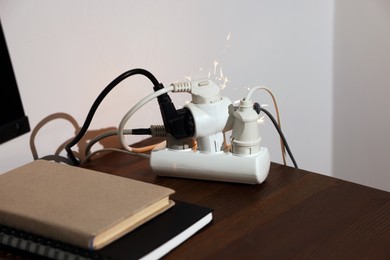 Photo of Inflamed plug in power strip indoors on wooden table. Electrical short circuit