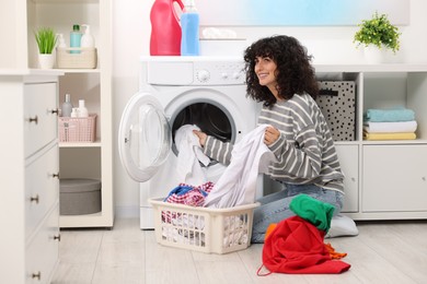 Happy woman putting laundry into washing machine indoors