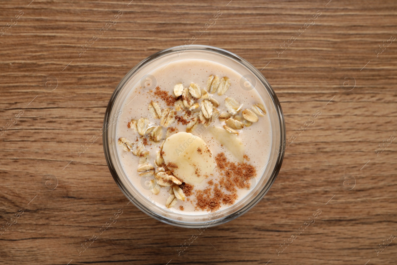 Photo of Glass of tasty banana smoothie with oatmeal and cinnamon on wooden table, top view