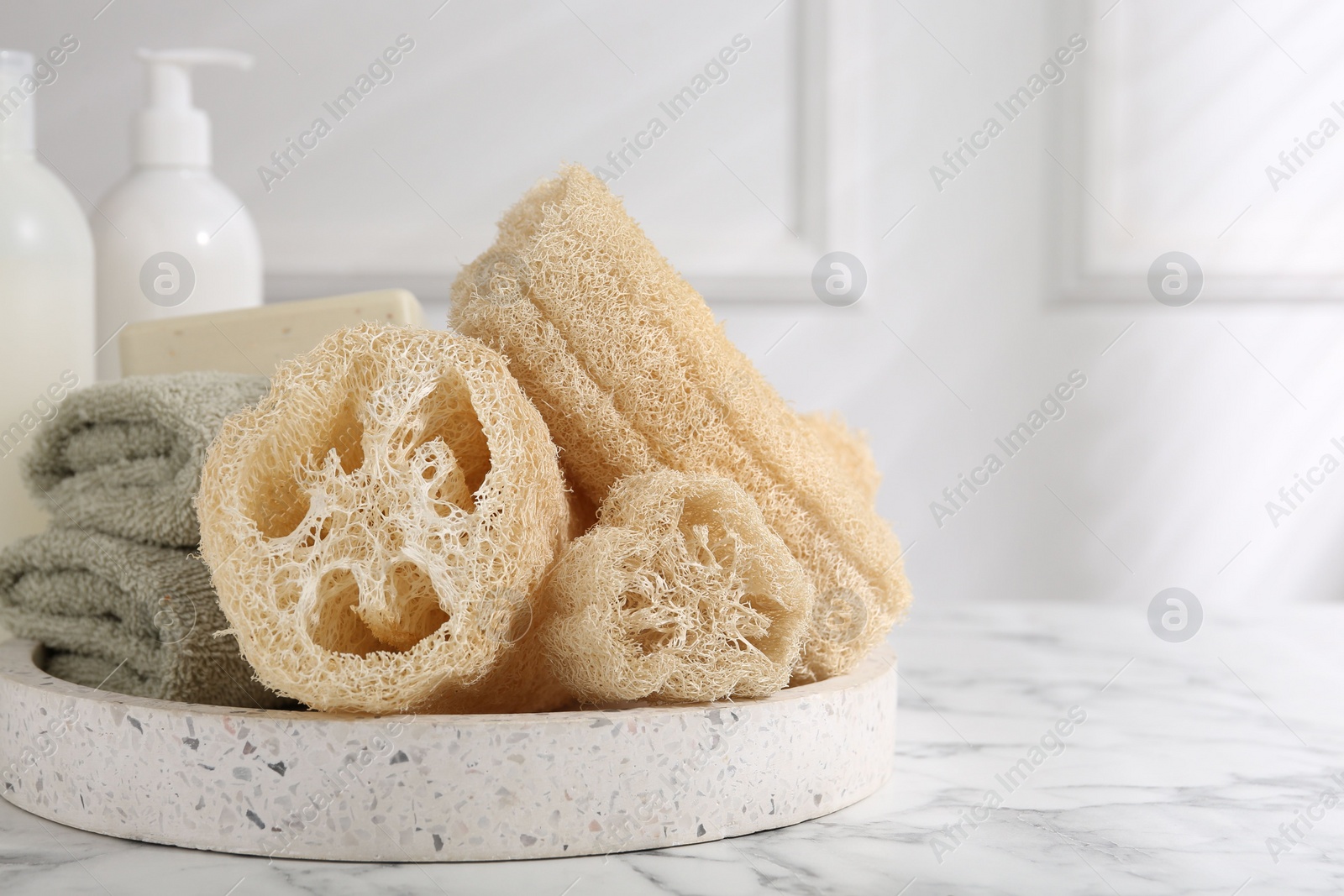 Photo of Loofah sponges, towels and soap on white marble table, space for text