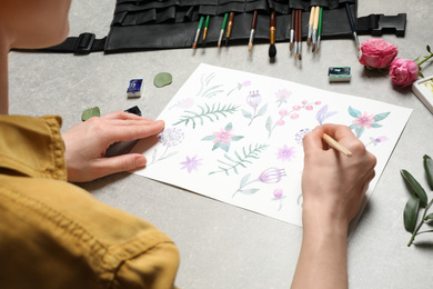 Photo of Woman painting flowers with watercolor at grey stone table, closeup