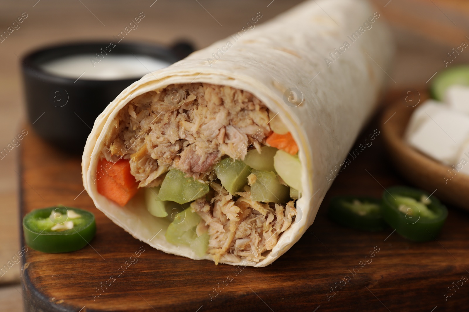 Photo of Delicious tortilla wrap with tuna and vegetables on wooden board, closeup