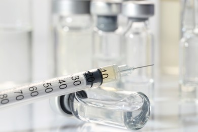 Photo of Glass vial and syringe with medication on white table, closeup