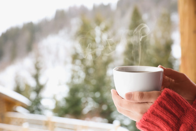 Photo of Woman with cup of tasty coffee outdoors on winter morning, closeup