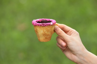 Photo of Woman holding delicious edible biscuit cupcoffee decorated with sprinkles outdoors, closeup