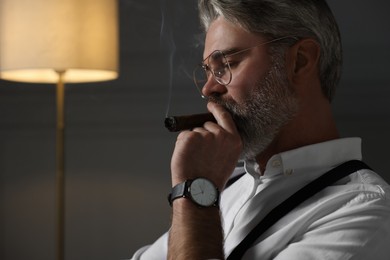 Photo of Bearded man smoking cigar at home. Space for text