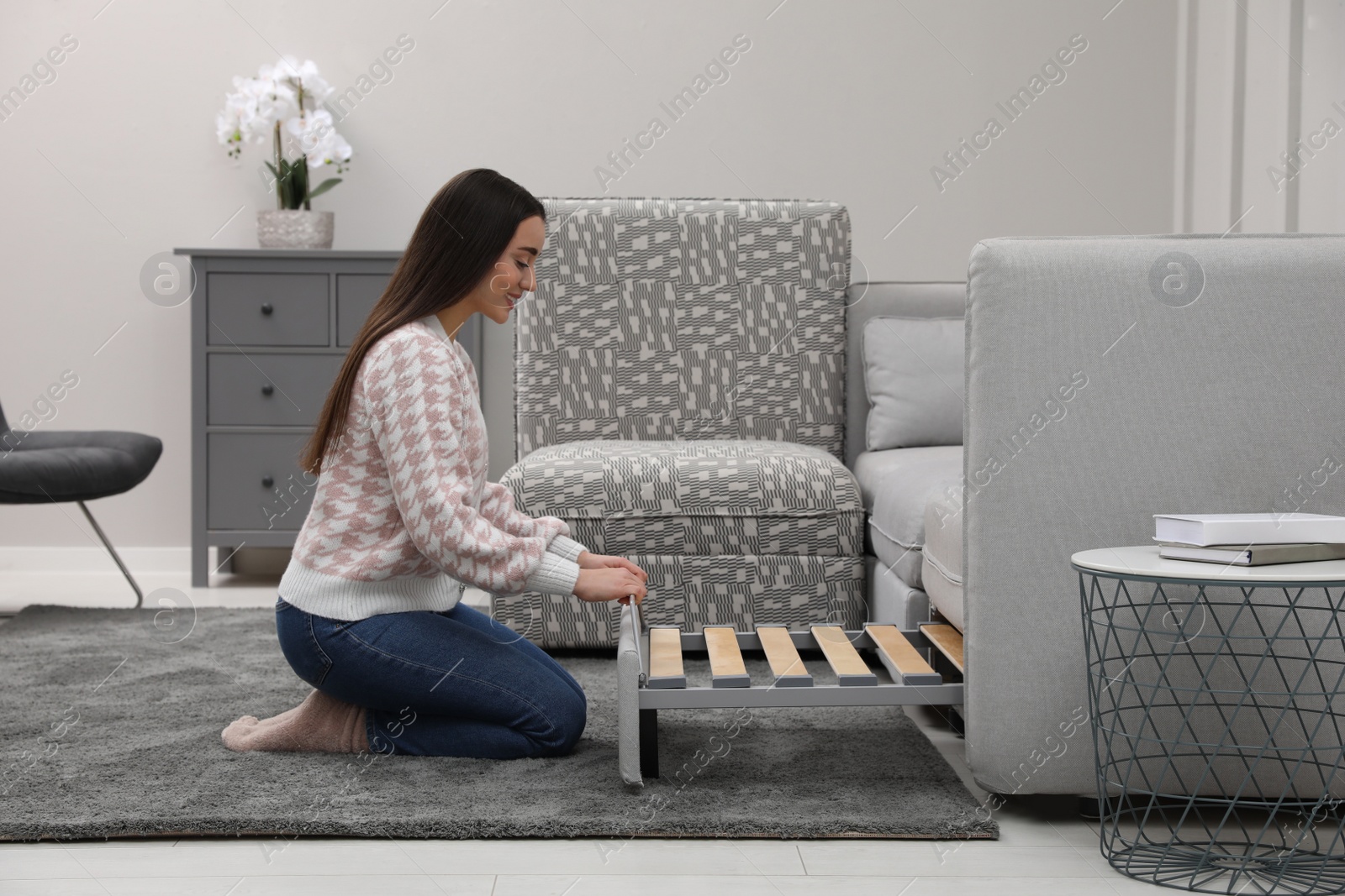 Photo of Woman making sleeping place for guest in living room. Convertible sofa