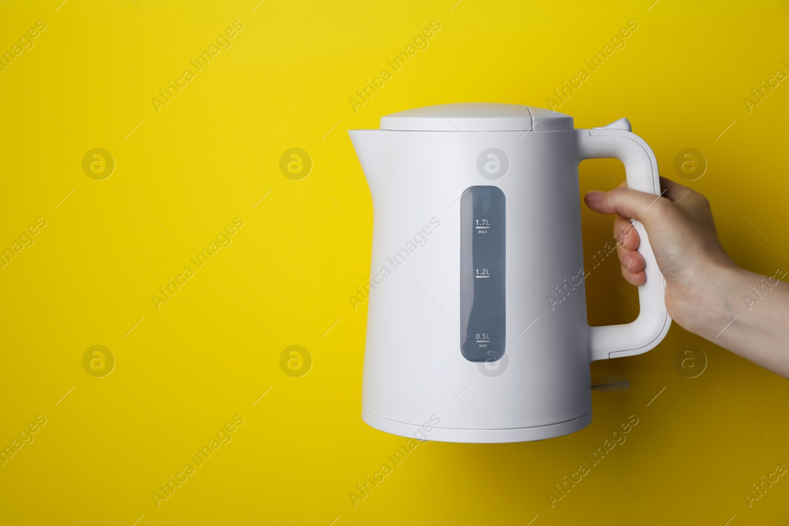 Photo of Woman holding modern electric kettle on yellow background, closeup. Space for text