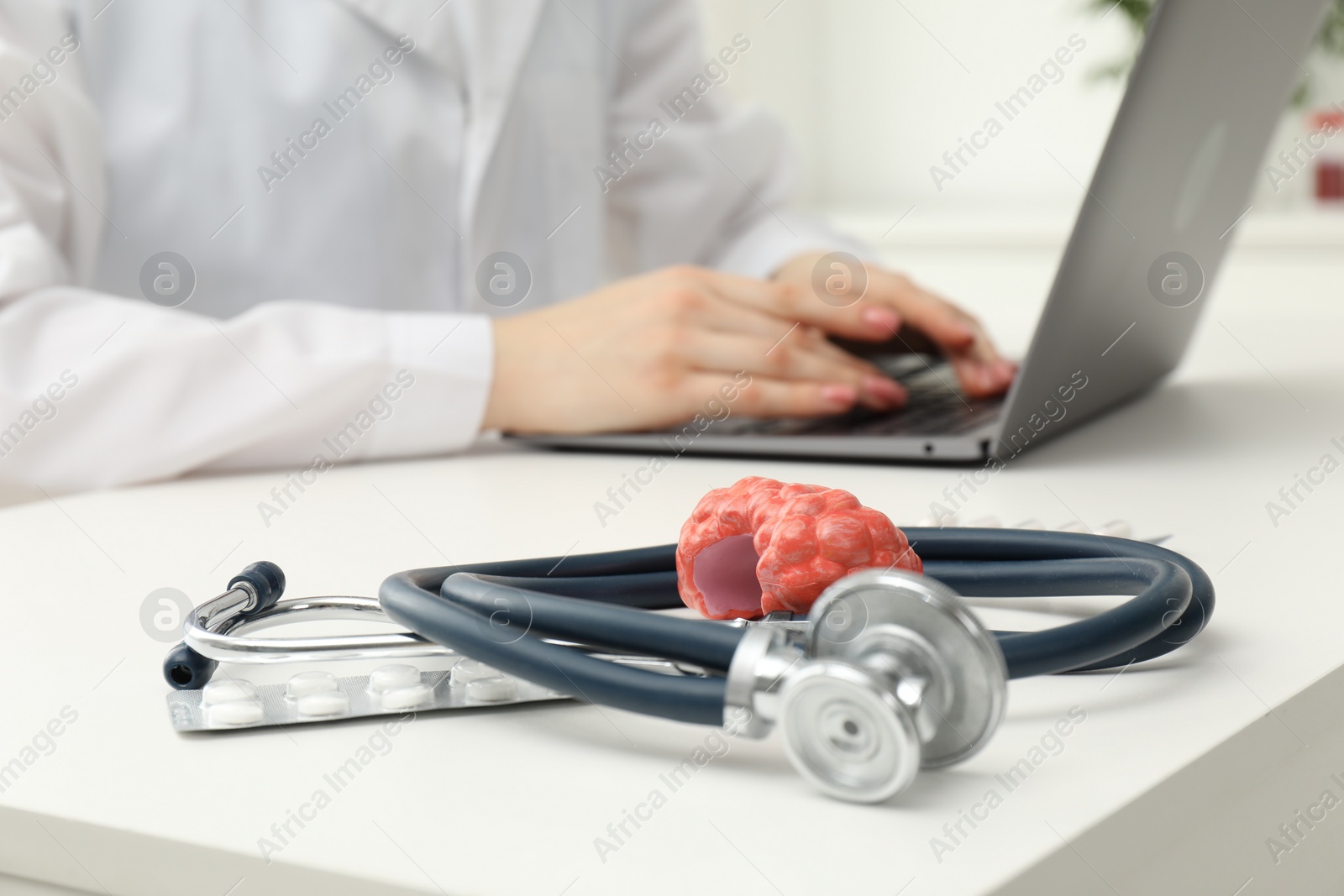 Photo of Endocrinologist working at table, focus on stethoscope and model of thyroid gland