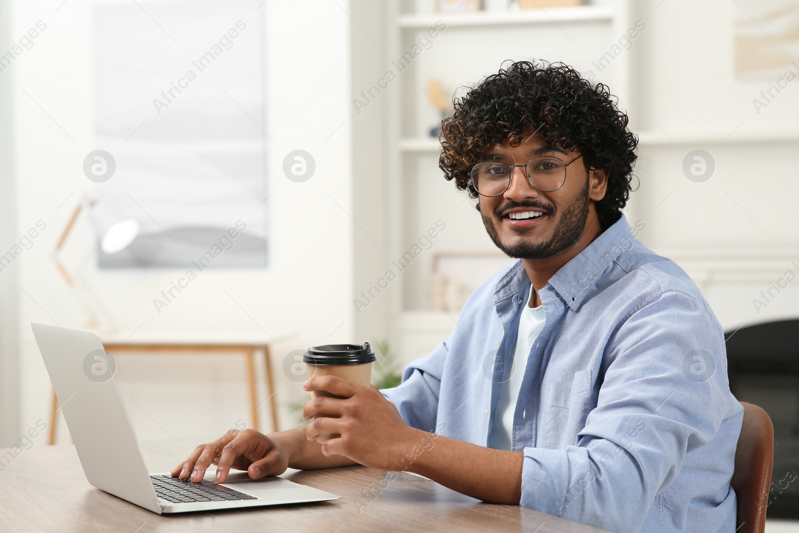 Photo of Handsome smiling man with coffee using laptop in room