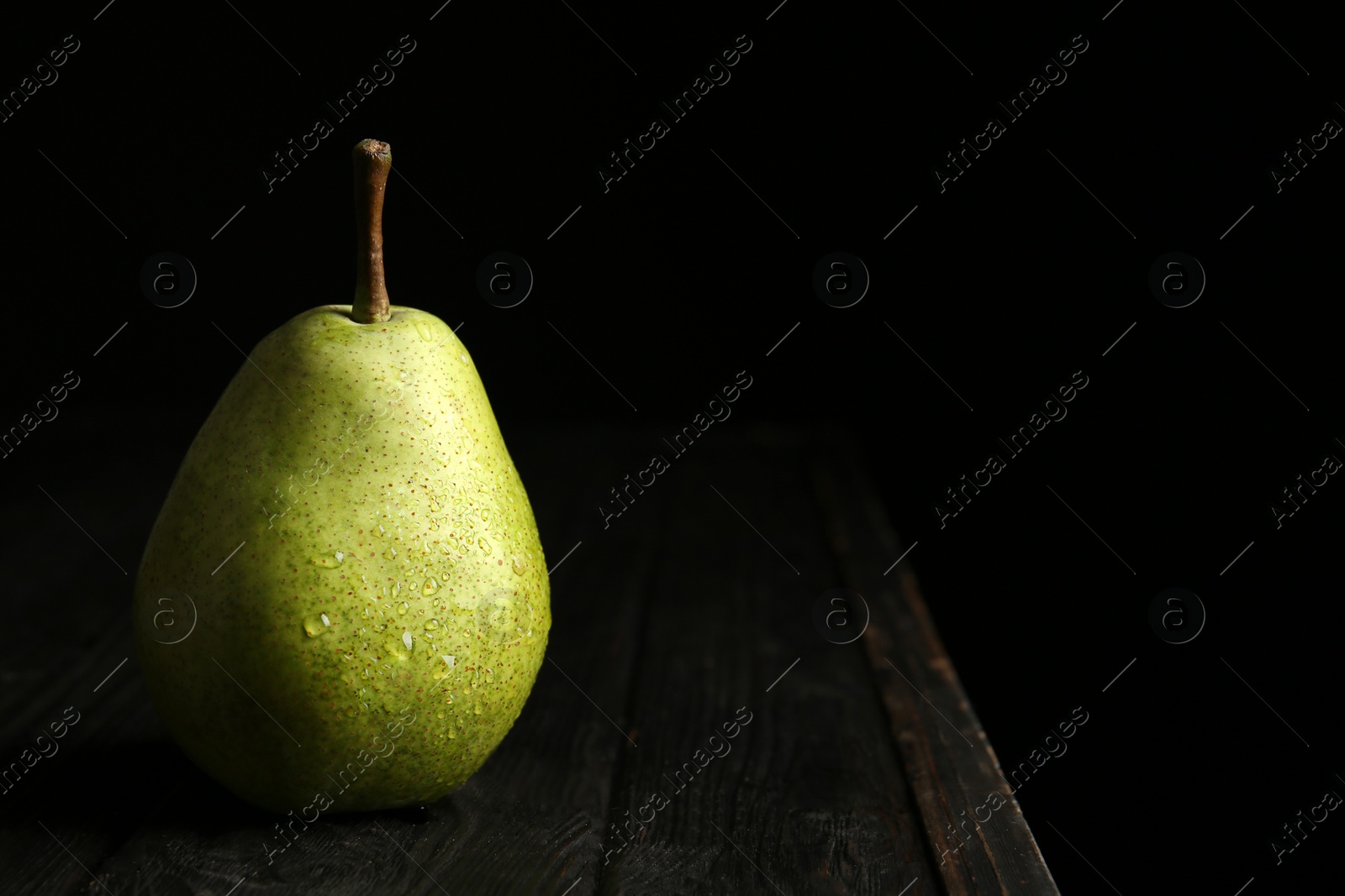 Photo of Ripe pear on wooden table against dark background. Space for text