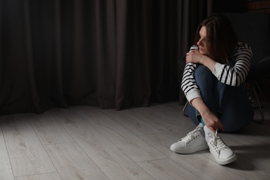 Photo of Sad young woman sitting on floor indoors, space for text