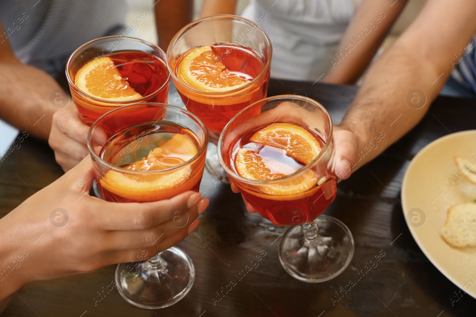 Photo of Friends with Aperol spritz cocktails together at wooden table, closeup