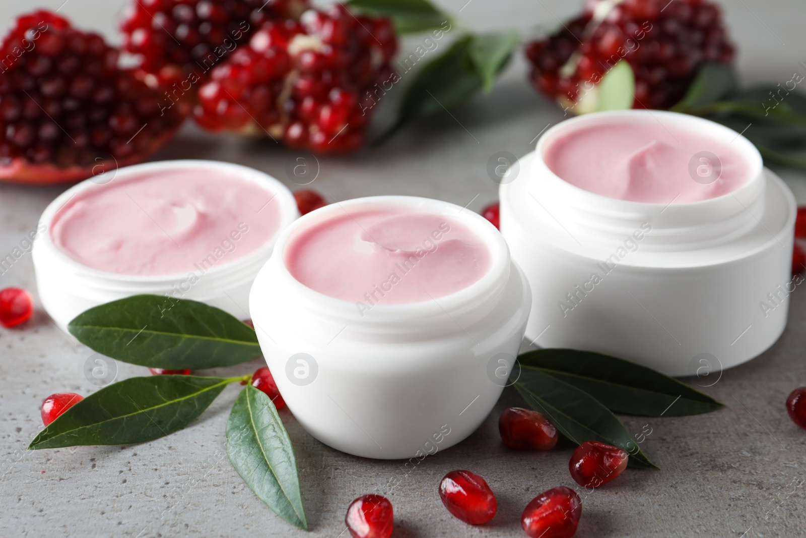 Photo of Natural facial mask, pomegranate seeds and green leaves on light grey table, closeup