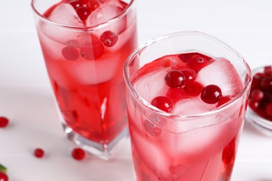 Tasty cranberry juice with ice cubes in glasses on white table, closeup