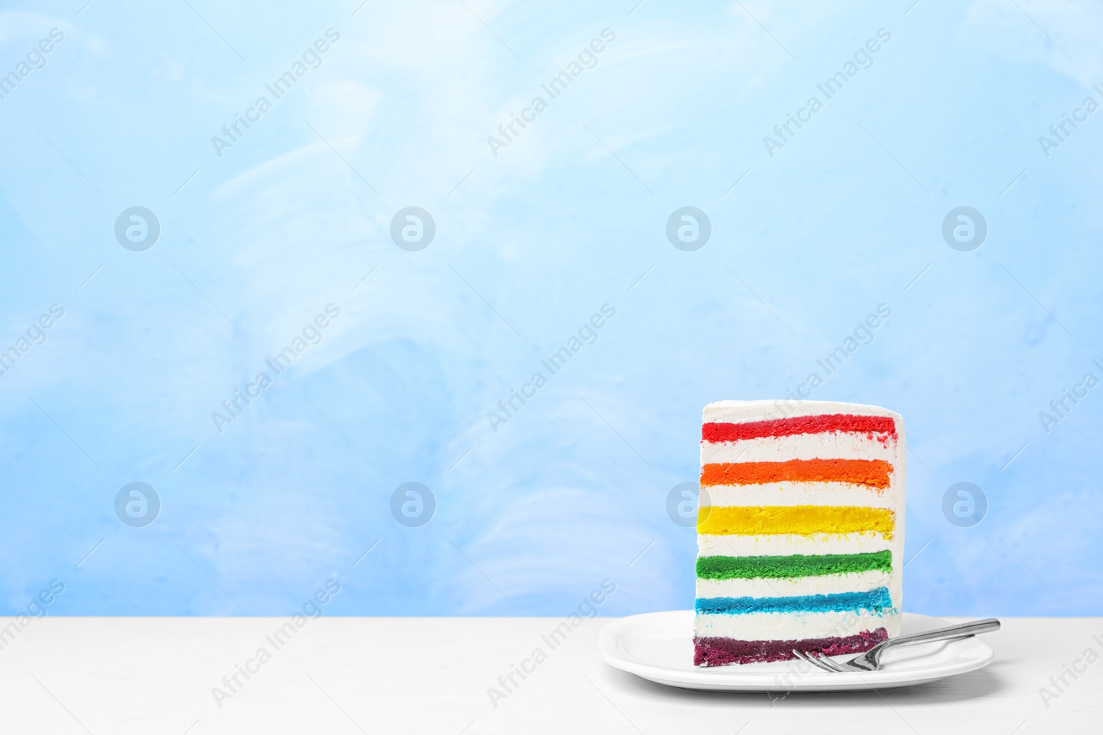 Photo of Plate with slice of delicious rainbow cake on table against color background