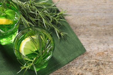 Glasses of refreshing tarragon drink with lemon slices on wooden table, flat lay. Space for text