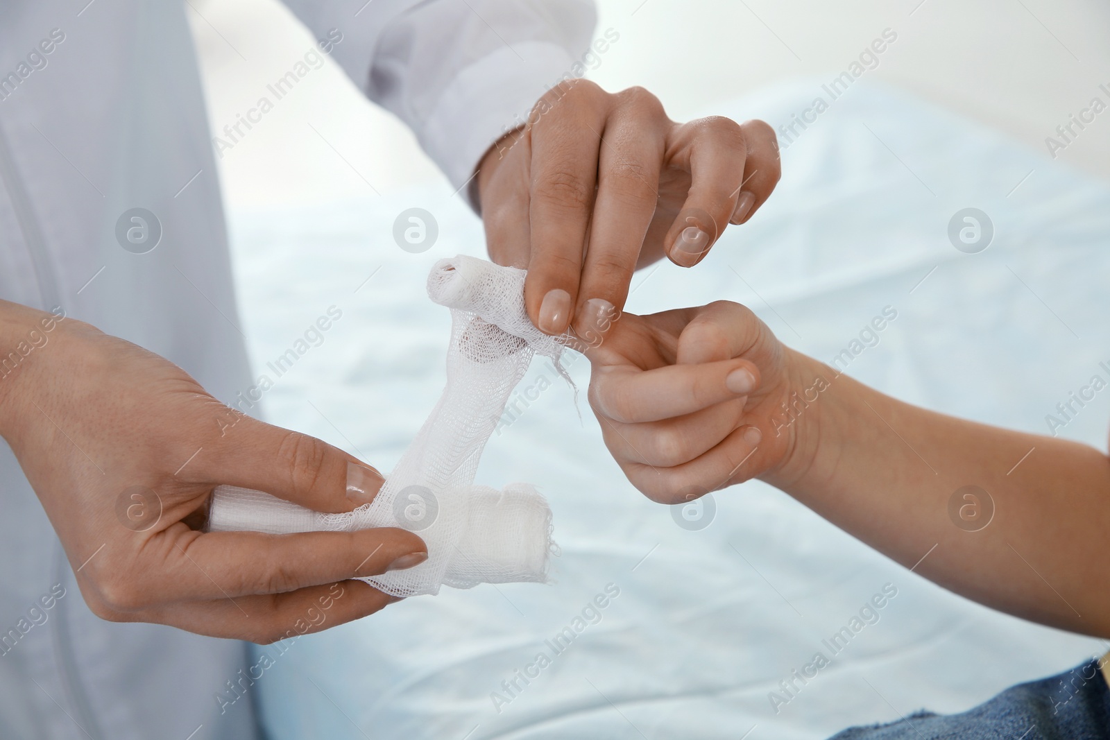 Photo of Female doctor applying bandage on little child's finger in clinic, closeup. First aid