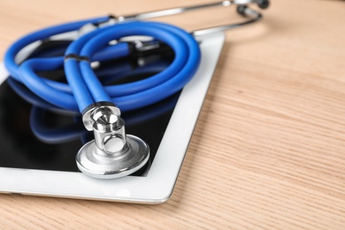 Photo of Stethoscope for checking pulse and tablet on wooden table, closeup. Space for text