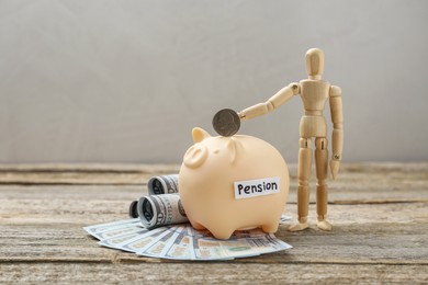 Photo of Mannequin putting coin into piggy bank with word Pension and dollar banknotes on wooden table. Retirement savings