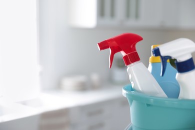 Photo of Plastic bucket with different cleaning supplies in kitchen, closeup. Space for text