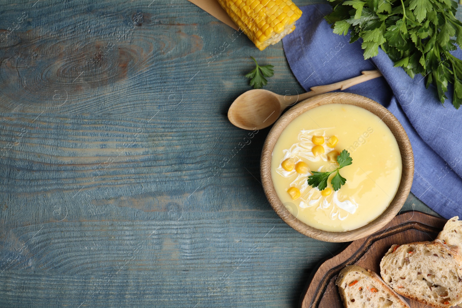 Photo of Delicious corn cream soup served on light blue wooden table, flat lay. Space for text