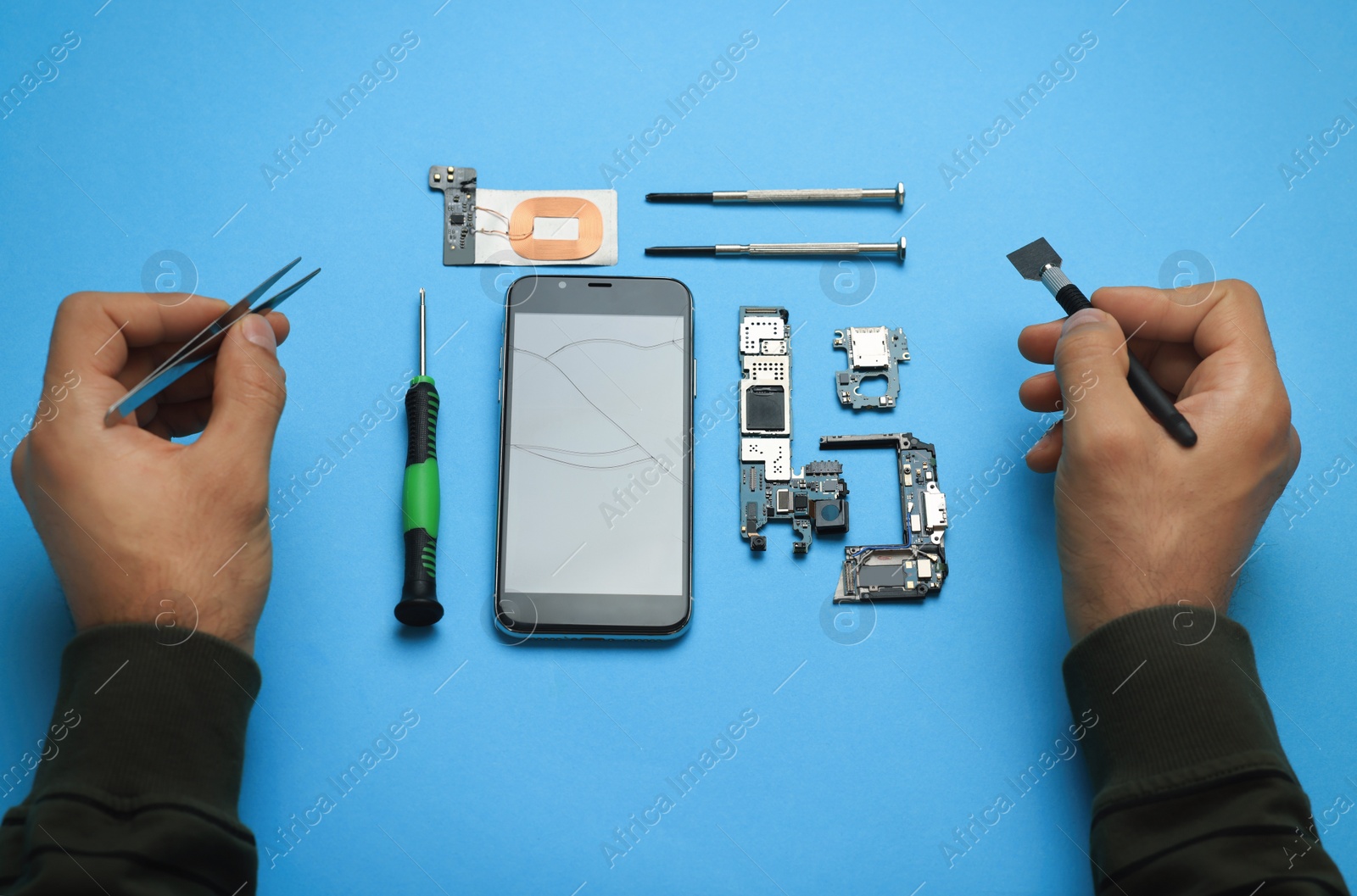 Photo of Man repairing broken smartphone on light blue background, above view