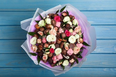 Photo of Beautiful bouquet of flowers and chocolate candies on light blue wooden table, top view