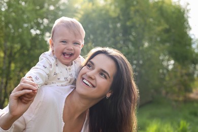 Photo of Happy mother playing with her cute baby in park on sunny day. Space for text