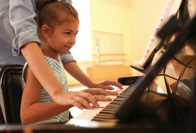 Photo of Young woman teaching little girl to play piano indoors