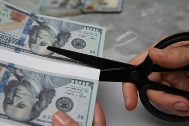 Photo of Counterfeiter cutting dollar banknotes with scissors at grey marble table, closeup. Fake money