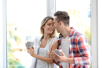 Photo of Happy young couple drinking morning coffee near window at home
