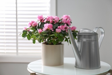 Photo of Beautiful Azalea flower in plant pot and watering can on white table indoors. House decor