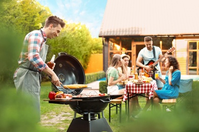 Photo of Group of friends at barbecue party outdoors. Young man near grill